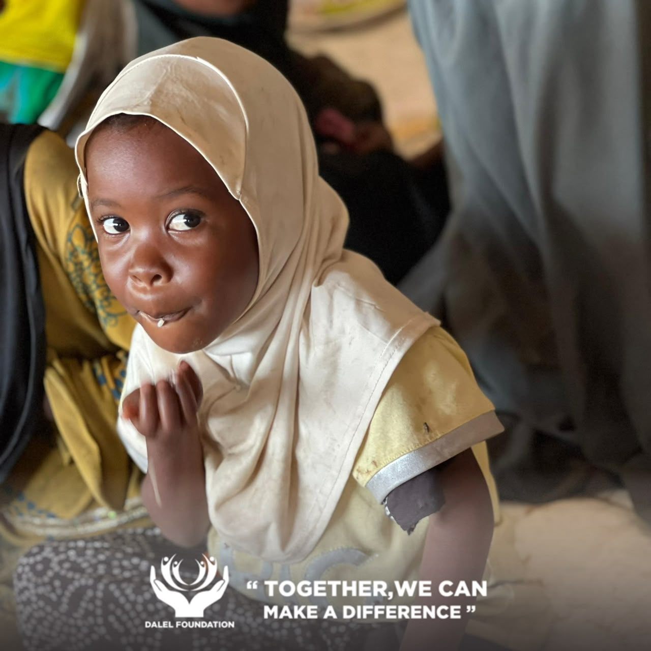A young girl in a cream headscarf looking up while eating a meal provided by Dalel Foundation
